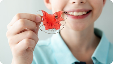 Smiling child holding a retainer