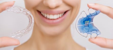 Smiling person holding a retainer and a clear aligner