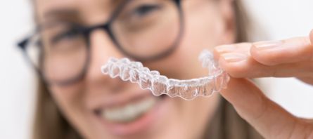 Smiling woman with glasses holding a clear aligner