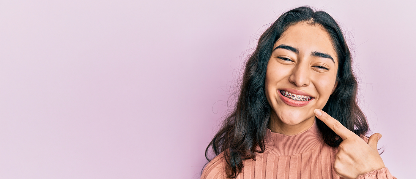 Young woman with traditional braces in Round Rock pointing to her smile